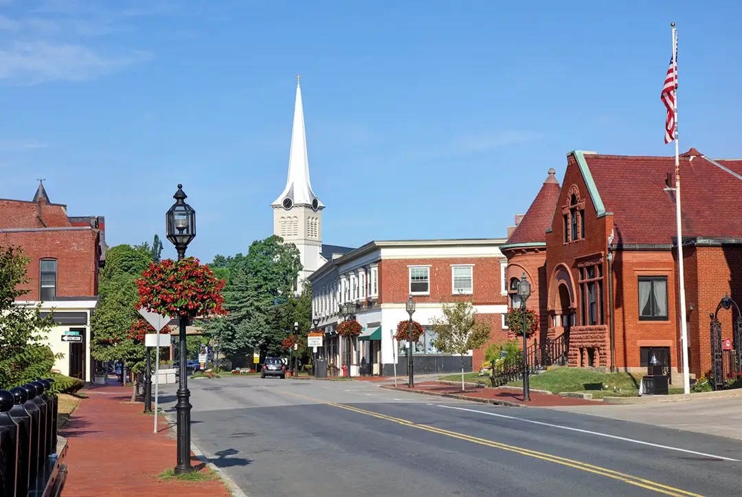 Scenic view of a small-town main street with historic brick buildings, a church steeple, and American flag, representing community growth and character.
