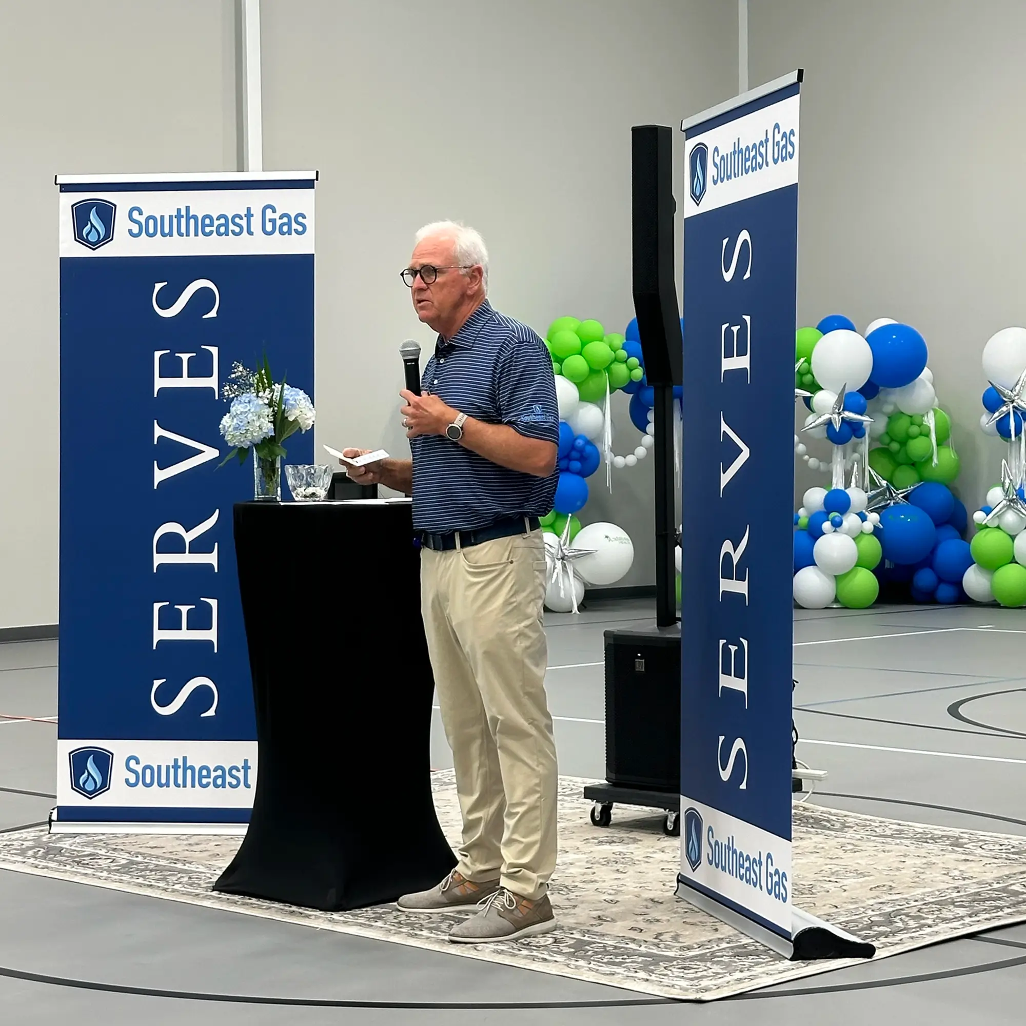 Southeast Gas CEO speaking at community event with SERVES banners and balloons.
