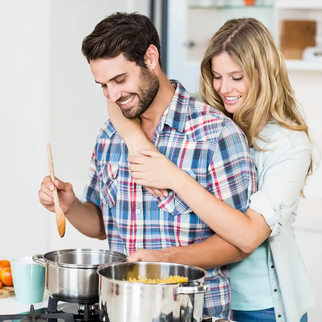 man cooking at a gas stove while his wife looks over his shoulder