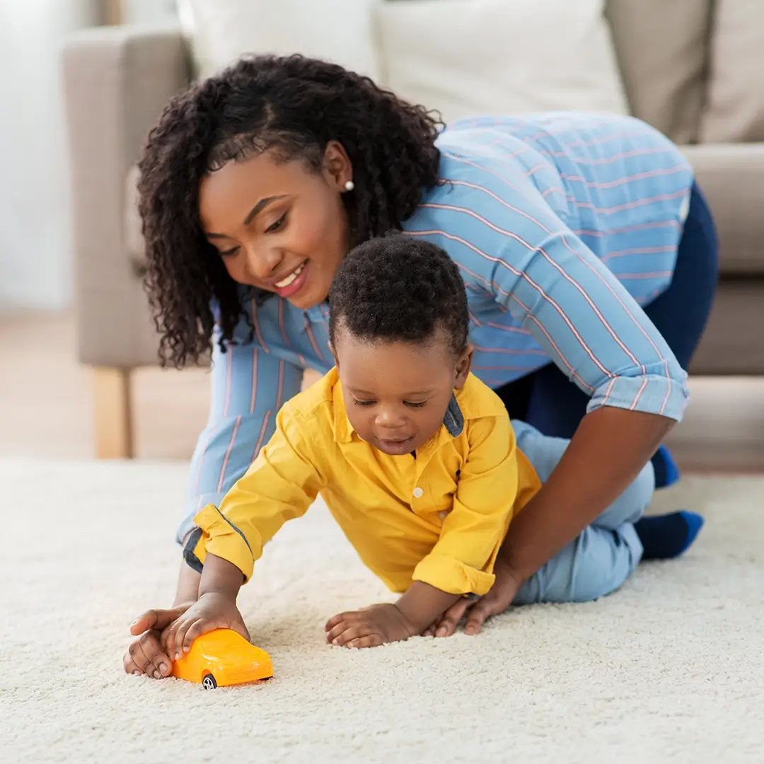 Mother and child playing with toy car on living room rug.